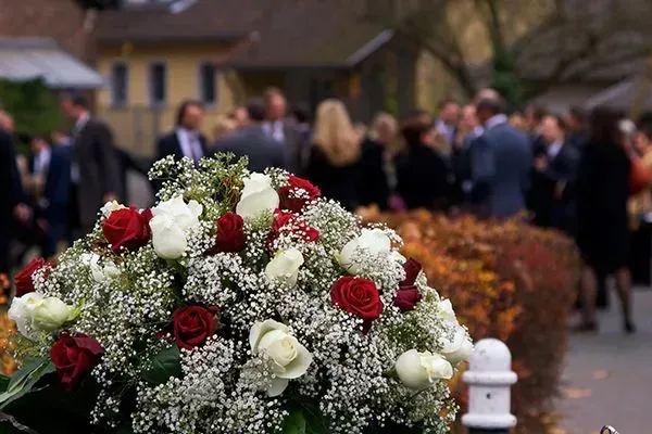 White and red flower wreath in a cemetery with people gathered in the background