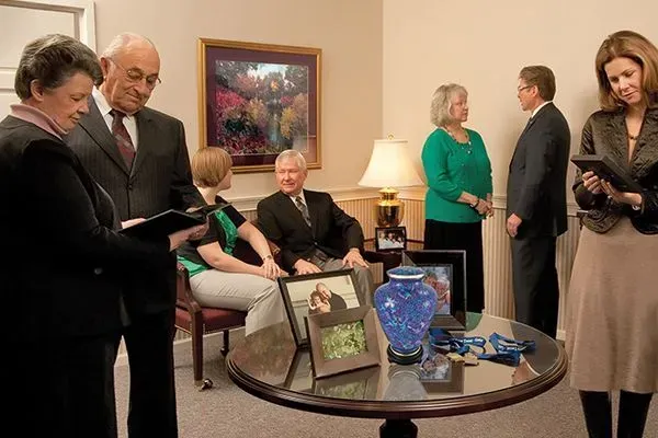 People mingling in a warmly lit living room, with framed art, a lamp, and a glass coffee table in the foreground