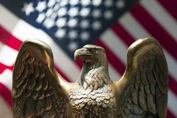 Bronze eagle statue in front of a blurred American flag background