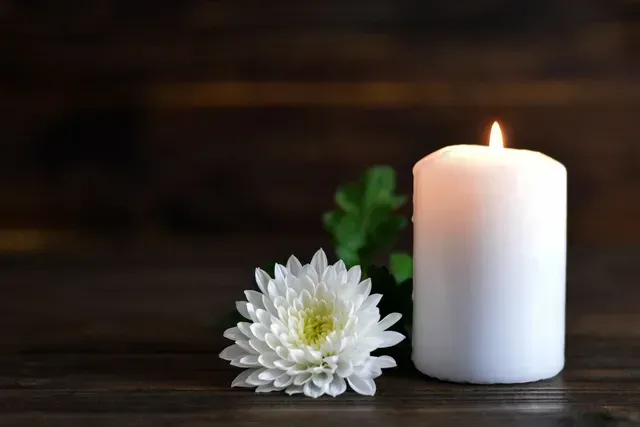 White candle and white flower on a dark wooden surface with a soft glowing flame