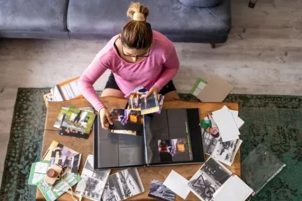 Person in a pink sweater sorting magazines on the floor beside an open binder and scattered papers.