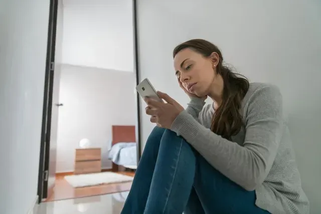 Woman sitting on the floor by a mirror, looking at her phone in a bright room