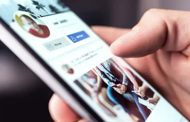 Hand tapping a smartphone screen showing a social media profile and photo feed
