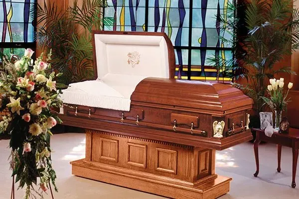 Wooden casket on a stand in a funeral chapel, with white upholstery and floral arrangements nearby