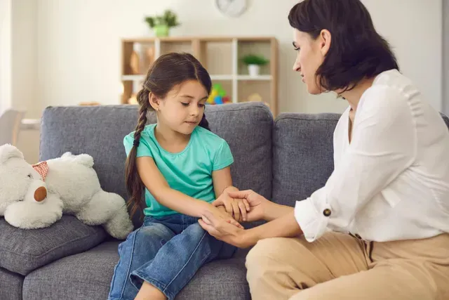 Woman comforting a child on a gray couch beside a white teddy bear