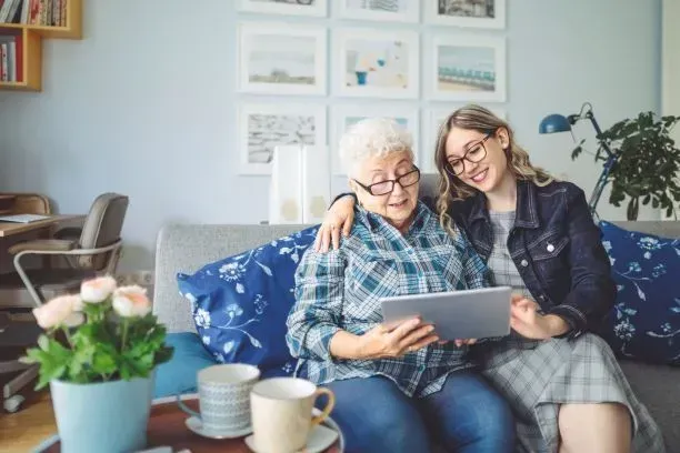 Two women on a couch looking at a tablet, with framed art on the wall and a coffee table in front.