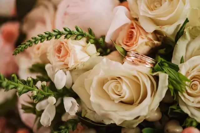 Cream and blush roses with greenery and gold wedding rings arranged in a romantic bouquet