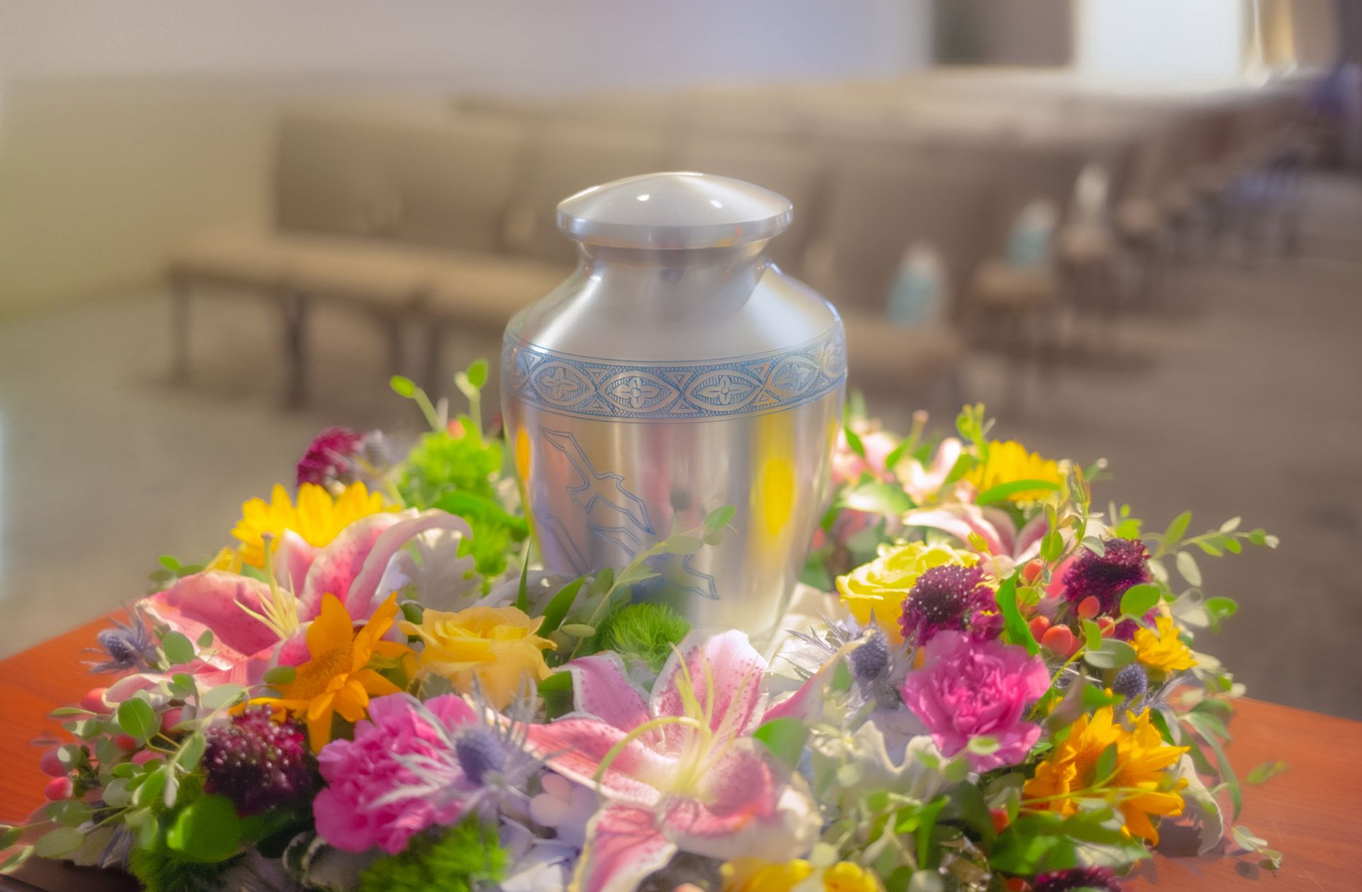 Silver urn surrounded by colorful flowers on a table in a softly lit room