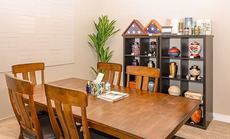 Dining room with wooden table and chairs, black shelving unit, and a potted plant against a light wall.