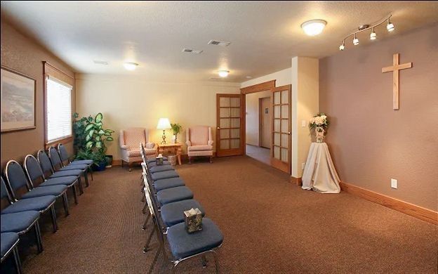 Empty chapel room with rows of chairs, a cross on the wall, and soft ceiling lights