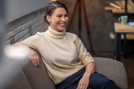 A woman in a sweater is sitting on a couch and smiling.