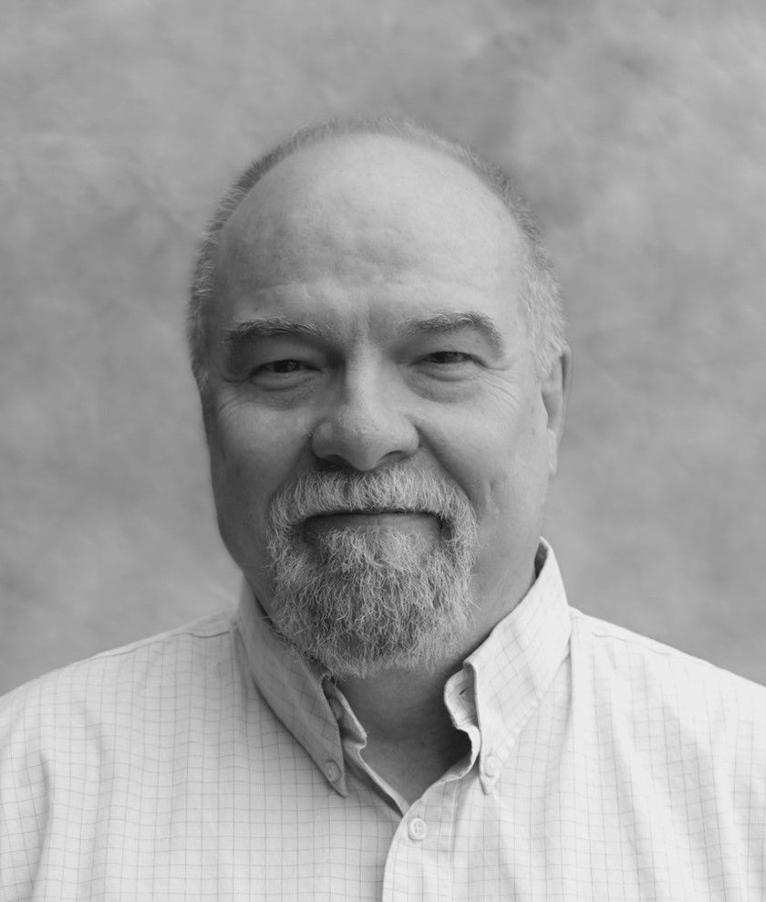 A black and white photo of a man with a beard wearing a plaid shirt.