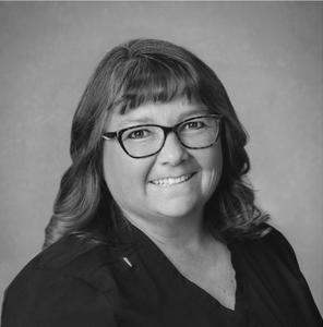 A woman wearing glasses and a black shirt is smiling in a black and white photo.