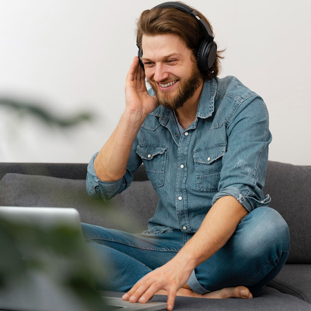 A man wearing headphones is sitting on a couch using a laptop