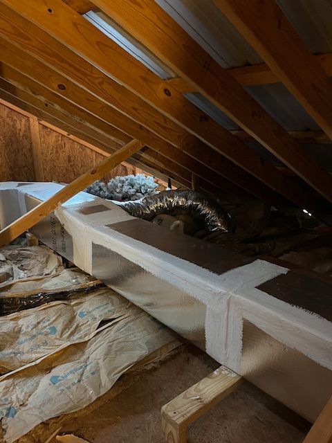 Attic interior with ductwork and insulation under wooden rafters.
