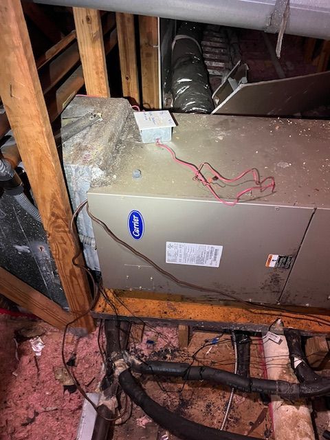 HVAC unit in attic: metal box with wires. Wooden beams and ductwork surround it.