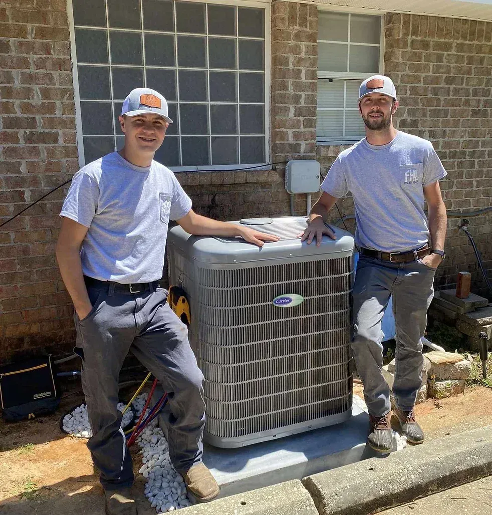 Two men are standing next to an air conditioner in front of a brick building.