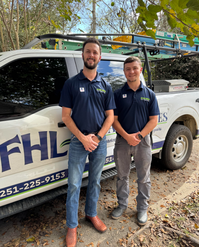 Two men are standing next to an air conditioner in front of a brick house.