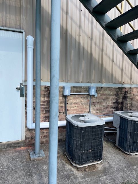 Exterior of a building with a white door, AC units, pipes, and stairs.