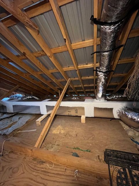 Interior view of an attic with wooden beams, metal roof, insulation, ductwork, and wooden supports.