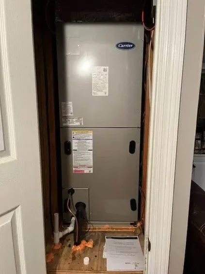 A carrier air conditioner is sitting in a closet next to a door.
