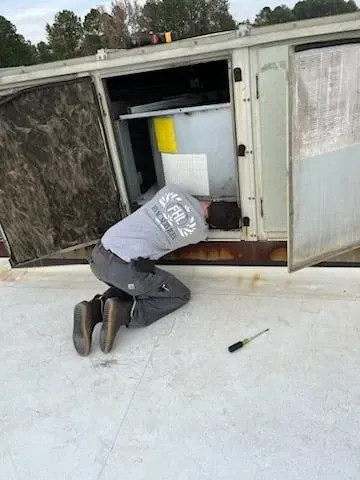 A man is kneeling down on the roof of a building looking into a box.