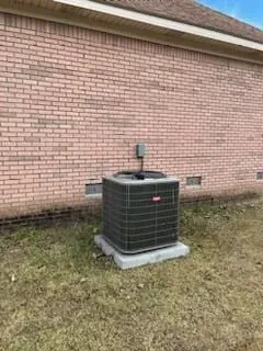 A large air conditioner is sitting in front of a brick building.