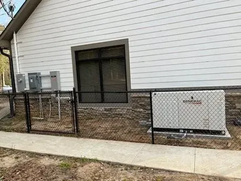 A white house with a black chain link fence and a generator in front of it.
