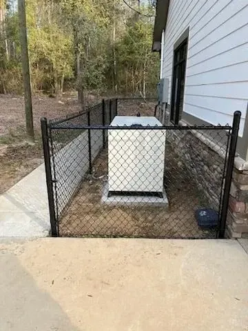 A generator is behind a chain link fence next to a house.