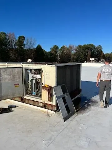 A man is walking on a roof next to an air conditioner.