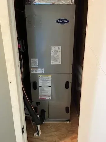 A carrier air conditioner is sitting in a closet next to a door.