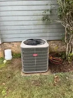 An air conditioner is sitting in the grass in front of a house.