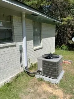 An air conditioner is sitting on the side of a white brick house.