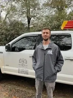 A man in a gray jacket is standing in front of a white truck.
