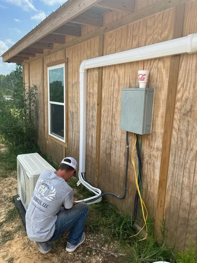 A man is working on an air conditioner outside of a house.