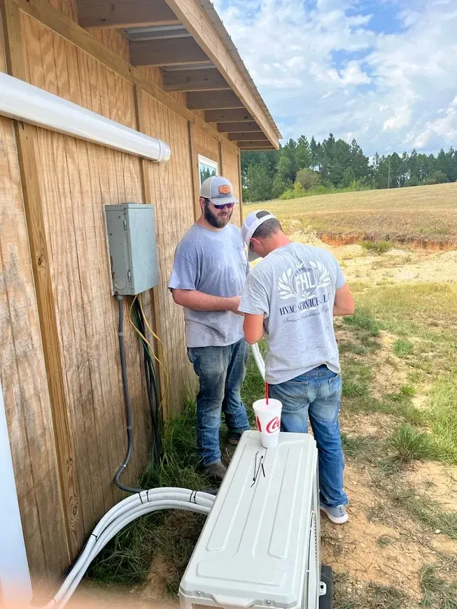 Two men are working on an air conditioner outside of a building.