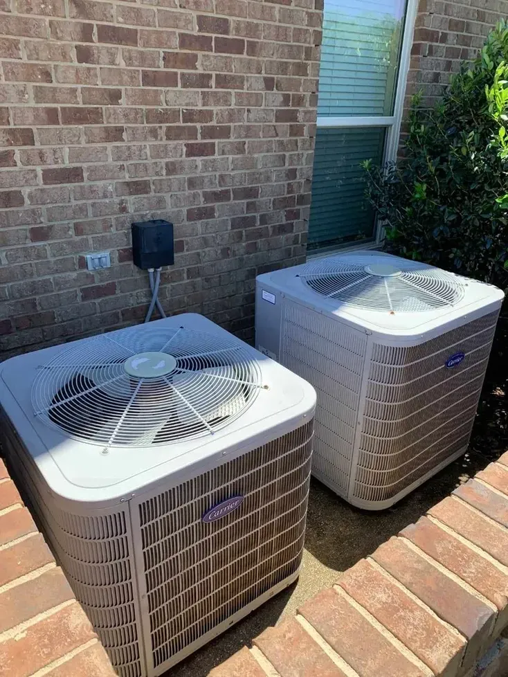 Two air conditioners are sitting on the side of a brick building.
