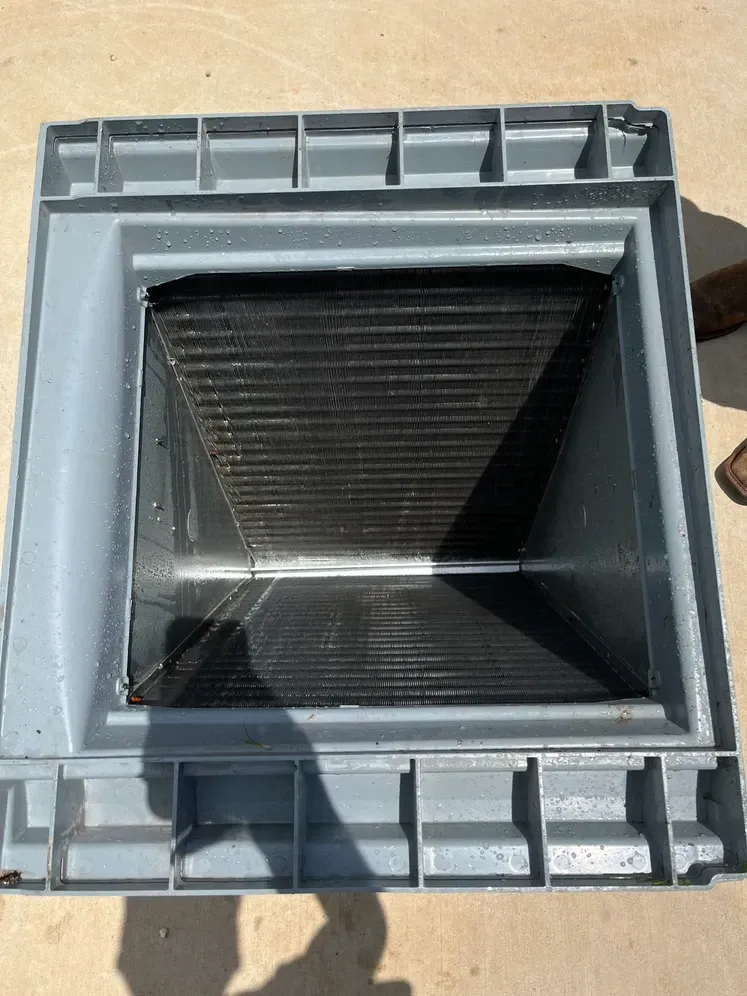 A gray plastic container with a black lid is sitting on a cement floor.