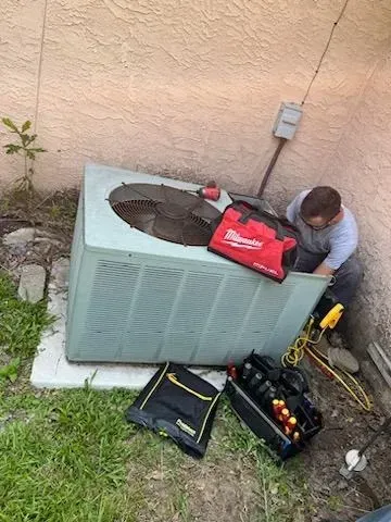 A man is working on an air conditioner outside of a house.