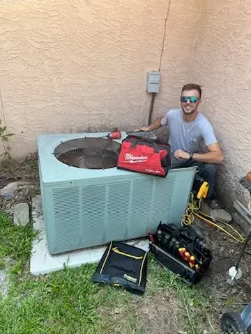 A man is sitting in front of an air conditioner.