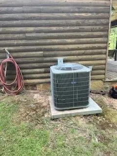 An air conditioner is sitting on a concrete platform in front of a log cabin.
