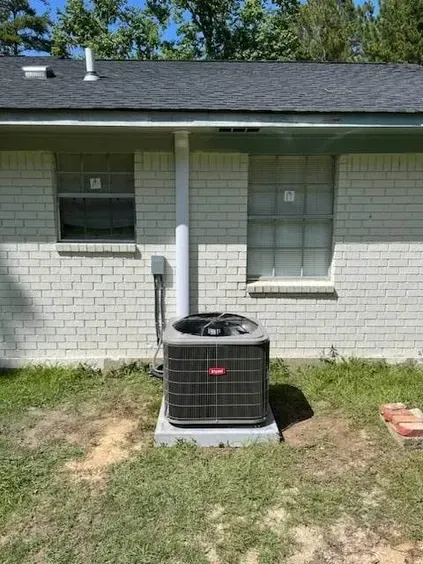 An air conditioner is sitting in the backyard of a white brick house.