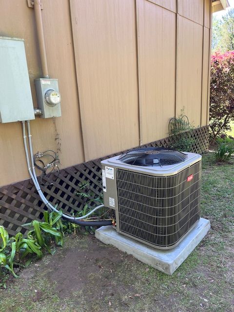AC unit on a concrete pad next to a tan house with electrical panel and meter.