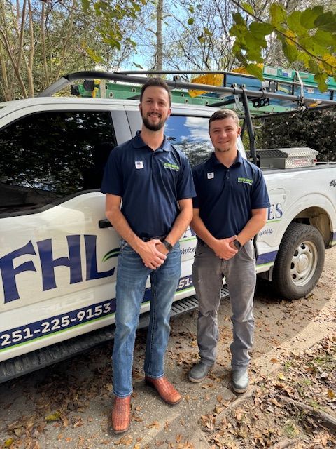 Two men in work attire stand by a truck with company logo, outdoors.