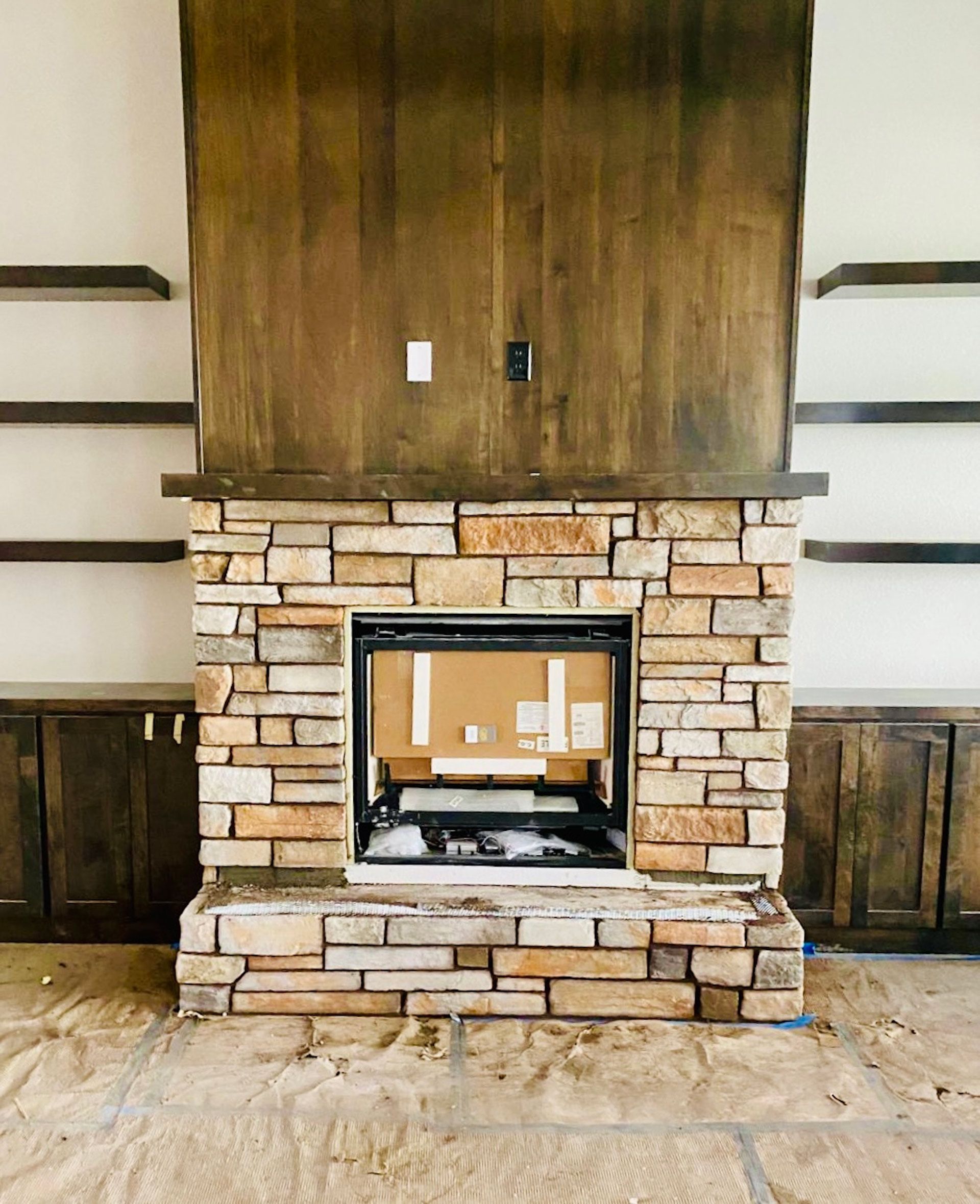 A living room with a stone fireplace and wooden shelves.