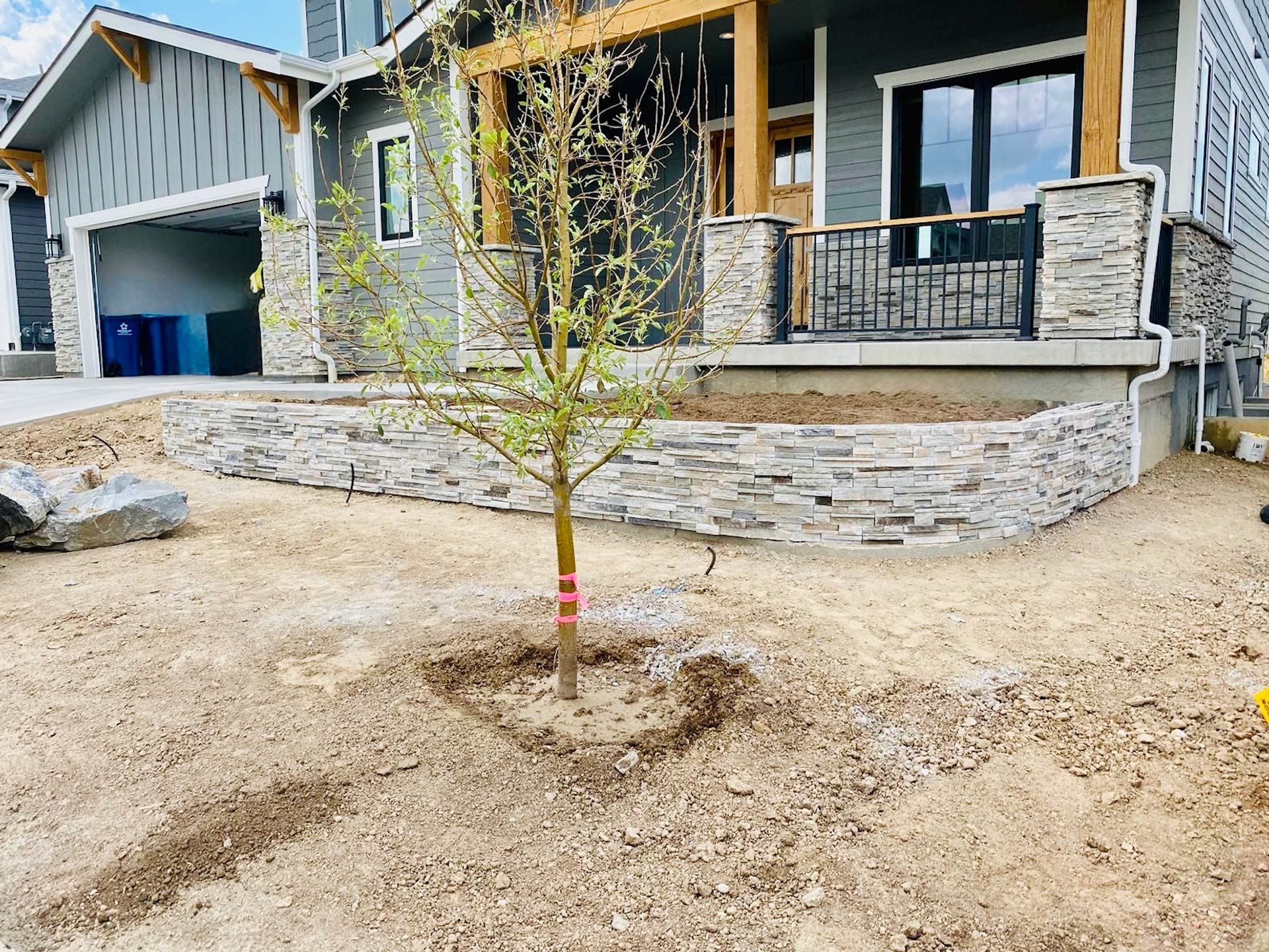 A house with a stone wall and a tree in front of it.