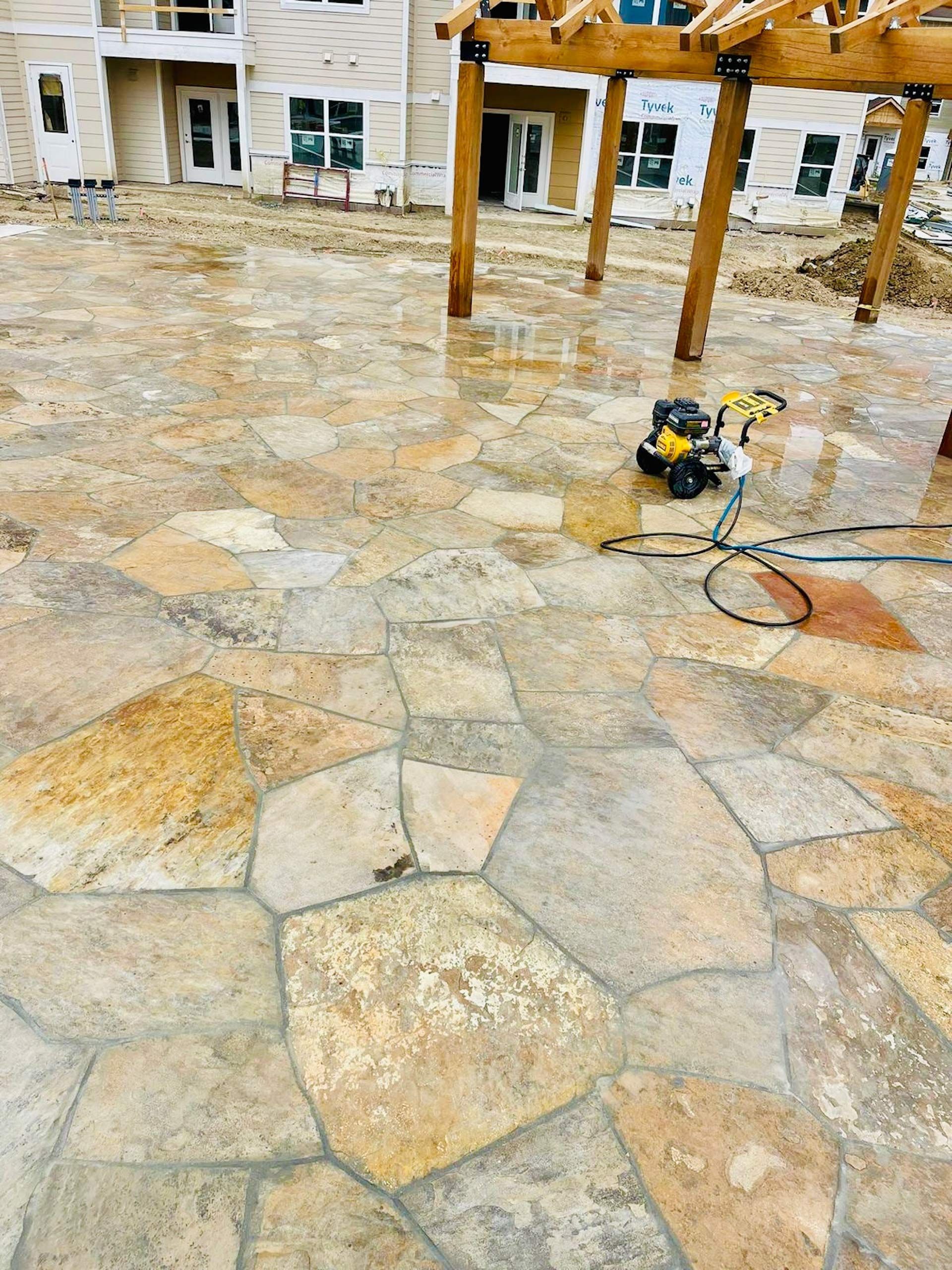 A large stone patio with a pergola and a hose.
