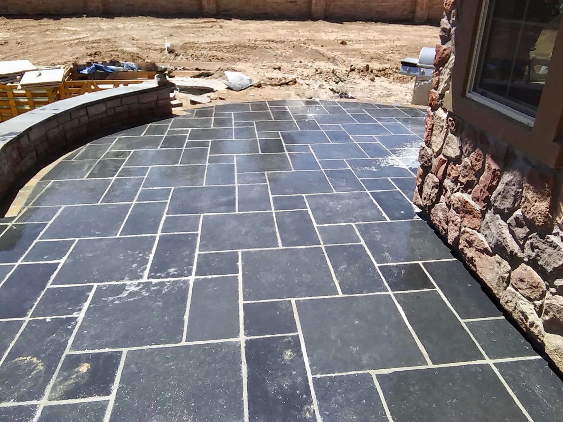A black tiled patio with a stone wall in the background