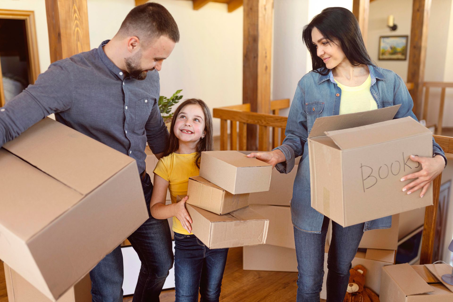 Family moving boxes into a new home. The parents and daughter hold several cardboard boxes.