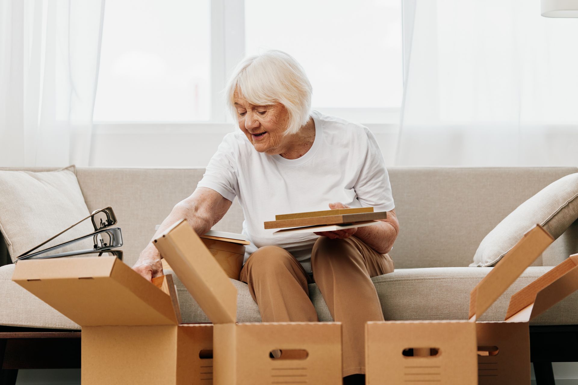 An elderly woman is sitting on a couch opening a cardboard box.